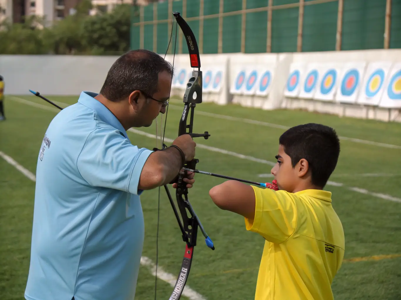 A close-up shot of an experienced archery coach providing personalized guidance to an archer during an advanced training session at the CLUB DES ARCHERS TULLISTES outdoor range.